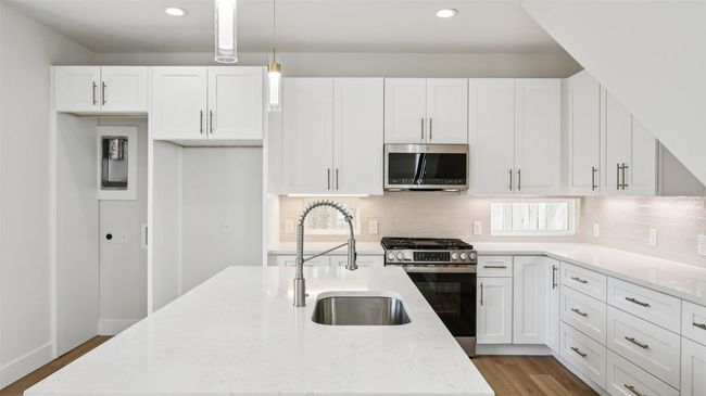 Kitchen with stainless steel appliances, white cabinets, light stone counters, light wood-style floors, and recessed lighting | Image 12