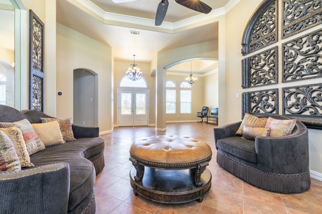 Tiled living area featuring arched walkways, crown molding, french doors, a ceiling fan, and a chandelier | Image 4