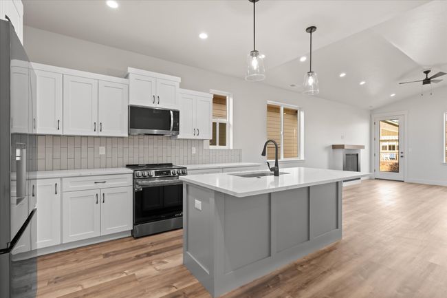 Kitchen featuring light wood finished floors, backsplash, vaulted ceiling, appliances with stainless steel finishes, and a sink | Image 9