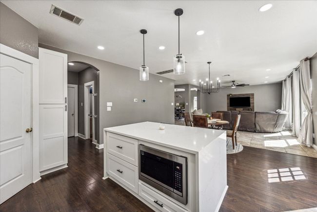 Kitchen with stainless steel microwave, white cabinets, arched walkways, dark wood finished floors, and visible vents | Image 13