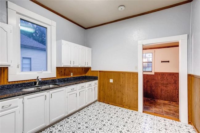 Kitchen featuring a sink, crown molding, white cabinetry, wainscoting, and wood walls | Image 12