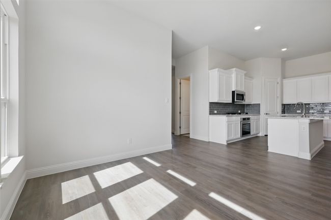 Kitchen with appliances with stainless steel finishes, white cabinets, light countertops, decorative backsplash, and dark wood-style flooring | Image 10