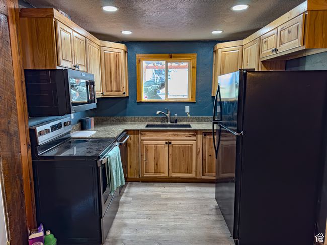 Kitchen with light wood-type flooring, sink, a textured ceiling, and black appliances | Image 5