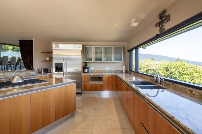 Kitchen with glass insert cabinets, a sink, built in appliances, light stone countertops, and modern cabinets | Image 11
