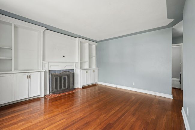 Unfurnished living room with a tiled fireplace, baseboards, and wood finished floors | Image 5