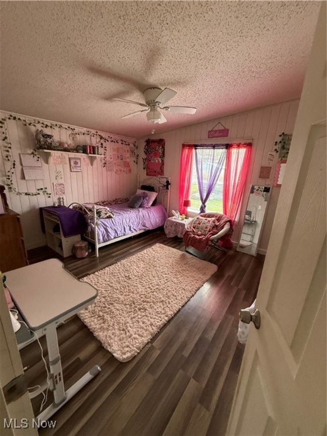 Bedroom with wooden walls, wood finished floors, a textured ceiling, and ceiling fan | Image 19