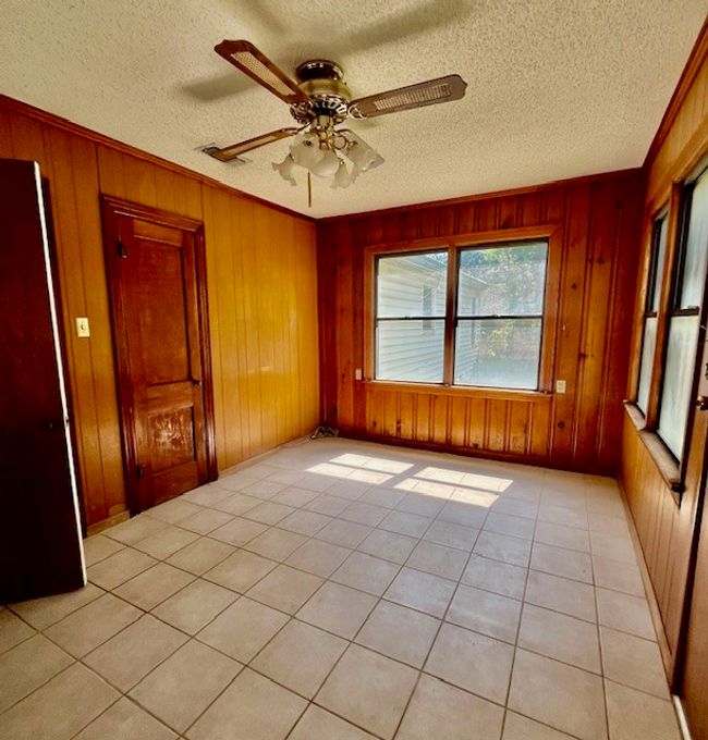 Empty room with wood walls, ceiling fan, a textured ceiling, light tile patterned floors, and ornamental molding | Image 7