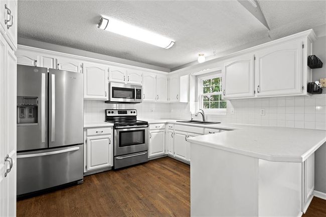 Kitchen with stainless steel appliances, a peninsula, white cabinets, dark wood-style flooring, and a textured ceiling | Image 11
