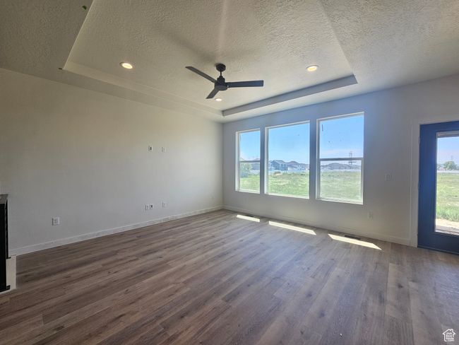 Empty room with a raised ceiling, a textured ceiling, wood finished floors, a ceiling fan, and baseboards | Image 9
