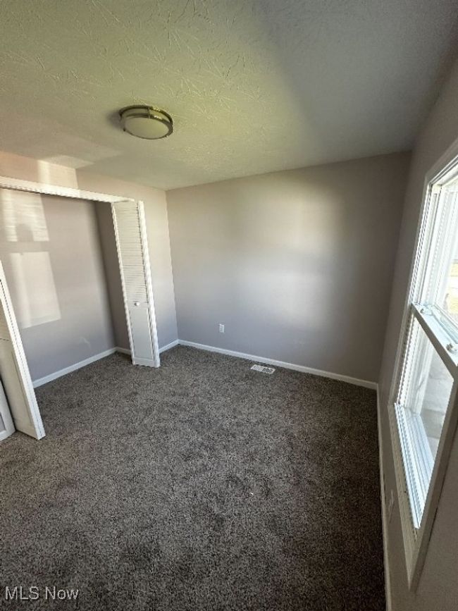 Unfurnished bedroom with dark carpet, a textured ceiling, and a closet | Image 7