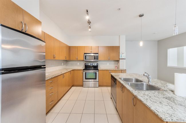 Kitchen with stainless steel appliances, decorative light fixtures, light tile patterned floors, track lighting, and light stone countertops | Image 5