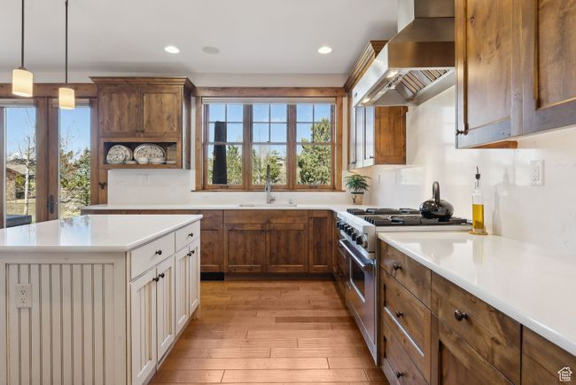 Kitchen with wall chimney range hood, stainless steel range, a sink, light countertops, and light wood-style flooring | Image 10