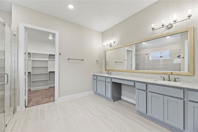 The owner’s ensuite will be easy to share with an extended dual-sink vanity, featuring plenty of counter space, stylish fixtures, and a seated makeup area. Also pictured here, a spacious walk-in closet offering built-in shelving to keep everything organized and within reach. | Image 30