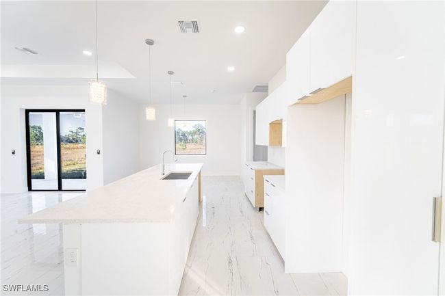 Kitchen with sink, a kitchen island with sink, hanging light fixtures, and white cabinets | Image 7