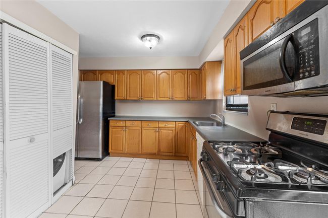 Kitchen featuring stainless steel appliances, a sink, brown cabinetry, and light tile patterned floors | Image 4