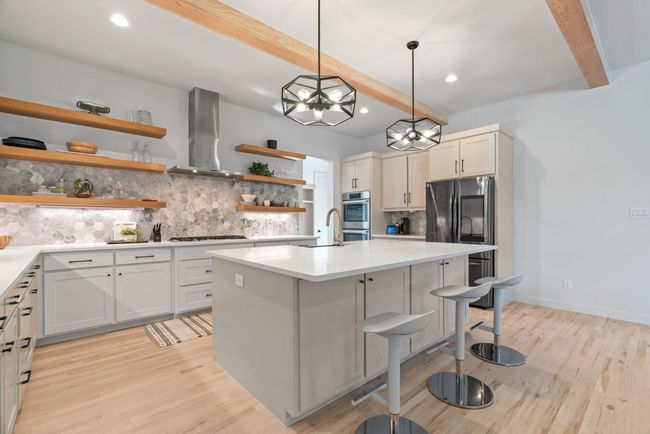 Kitchen featuring wall chimney exhaust hood, open shelves, appliances with stainless steel finishes, beam ceiling, and tasteful backsplash | Image 14