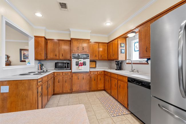 Kitchen featuring appliances with stainless steel finishes, brown cabinetry, light countertops, and crown molding | Image 11