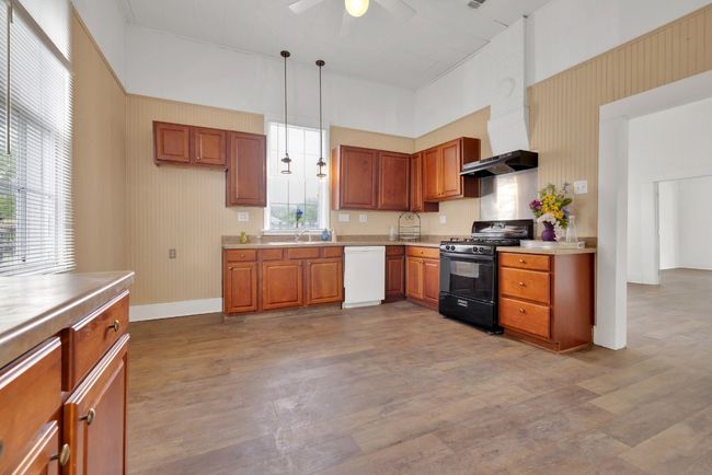 Kitchen with black gas range oven, wood finished floors, wall chimney range hood, a ceiling fan, and white dishwasher | Image 11