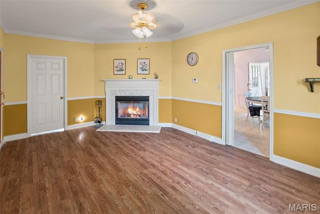 Unfurnished living room featuring a ceiling fan, wood finished floors, a glass covered fireplace, and crown molding | Image 17