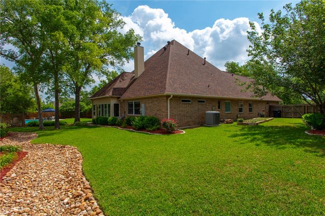 Back of property featuring central AC unit, a fenced backyard, roof with shingles, a lawn, and brick siding | Image 37