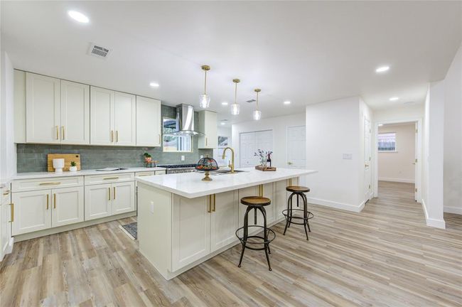 The island kitchen is a stunning focal point, fully renovated with Quartz countertops and a modern green subway tile backsplash that adds a pop of color. The spacious island provides ample counter space for meal prep and doubles as a casual dining area with seating. | Image 10