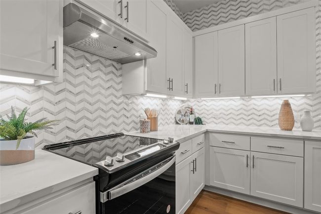 Kitchen with white cabinets, light countertops, under cabinet range hood, and electric stove | Image 13