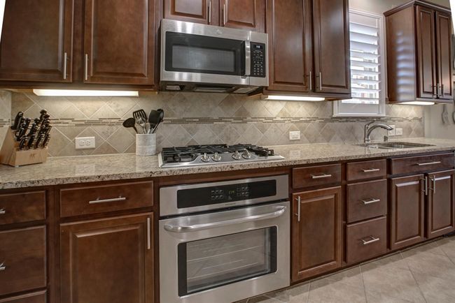 Kitchen featuring appliances with stainless steel finishes, light stone counters, light tile patterned floors, and tasteful backsplash | Image 7
