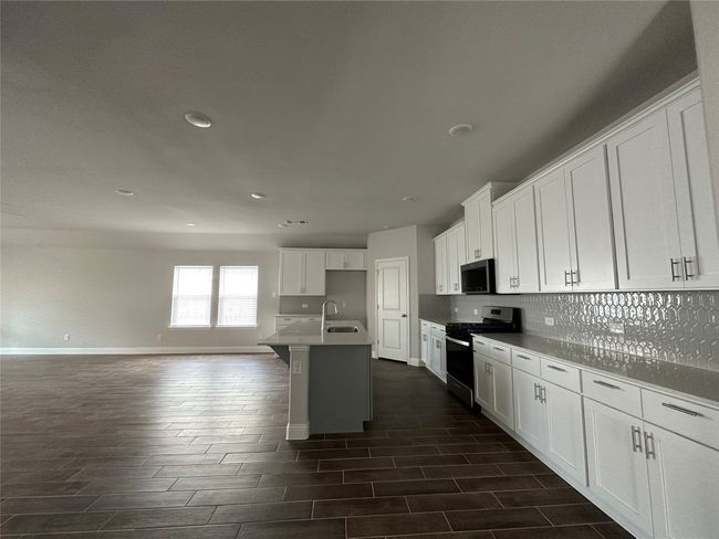 Kitchen featuring stainless steel gas stove, open floor plan, backsplash, recessed lighting, and white cabinetry | Image 5