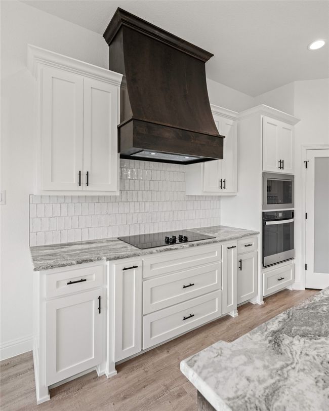 Kitchen with wall oven, custom exhaust hood, stainless steel microwave, white cabinets, and recessed lighting | Image 19