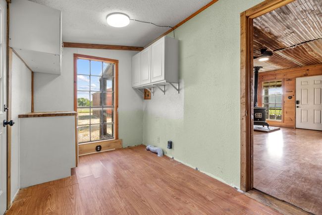 Laundry room featuring a wood stove, light wood-style flooring, a textured wall, and cabinet space | Image 26