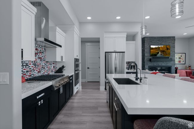 Kitchen featuring wall chimney range hood, stainless steel appliances, dark cabinetry, a sink, and light countertops | Image 16