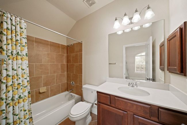 This bathroom features a clean, modern design with a tiled shower and bathtub, a large mirror, and ample lighting. The vanity offers storage space with wooden cabinets. | Image 30