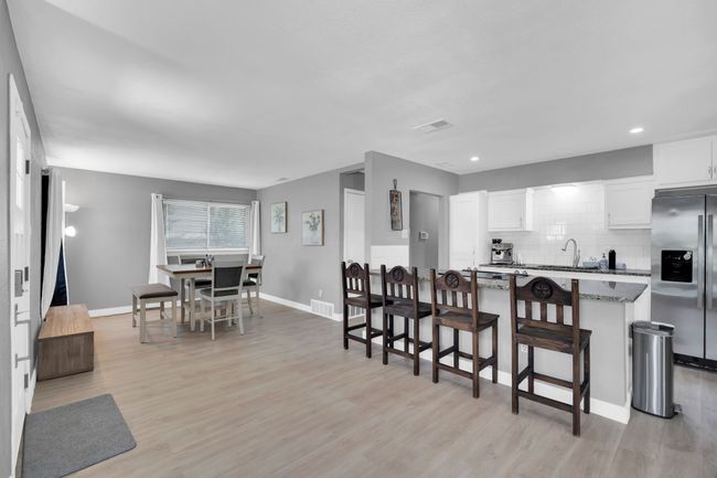 Kitchen featuring decorative backsplash, light wood-style flooring, a breakfast bar, white cabinetry, and stainless steel fridge with ice dispenser | Image 7