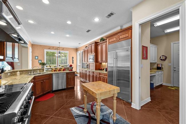 Cherry-stained cabinetry stretches wall-to-wall, flanked by granite counters, under-cabinet lighting and a built-in Sub-Zero refrigerator—pantry access just beyond. And a floor outlet under the portable island. | Image 16