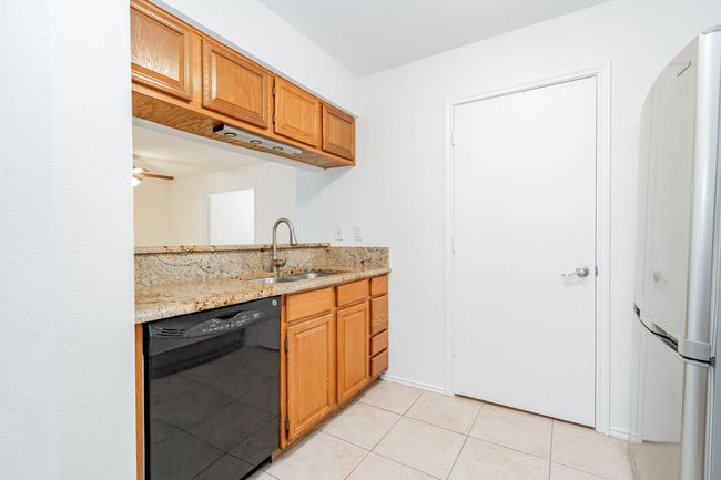 Kitchen with light tile patterned floors, black dishwasher, a sink, freestanding refrigerator, and brown cabinets | Image 27