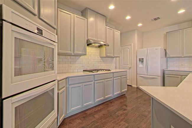 Kitchen with white appliances, under cabinet range hood, light countertops, recessed lighting, and tasteful backsplash | Image 16