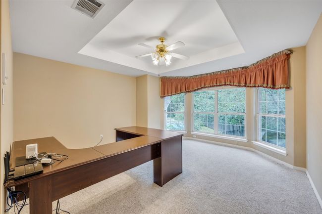 Carpeted office space featuring a tray ceiling and a ceiling fan | Image 30