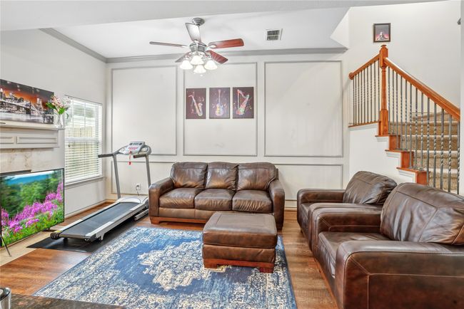 Living room with wood finished floors, a ceiling fan, crown molding, a decorative wall, and stairs | Image 7