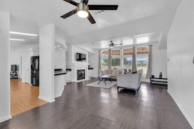 Living area featuring a ceiling fan, dark wood-type flooring, and a glass covered fireplace | Image 9