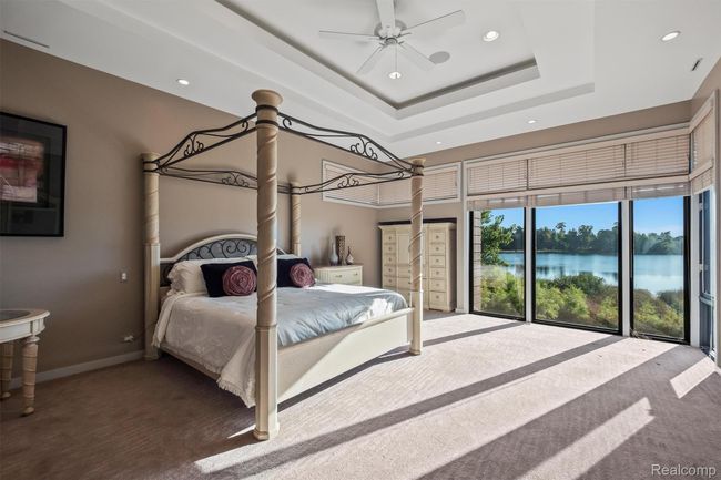 Carpeted bedroom featuring a water view, a raised ceiling, recessed lighting, a ceiling fan, and a high ceiling | Image 20