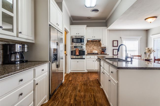 The kitchen has been thoughtfully updated with granite countertops, classic beadboard cabinetry, a large center island with built-in sink, and stainless steel appliances—including gas cooktop, built-in oven and microwave. | Image 10