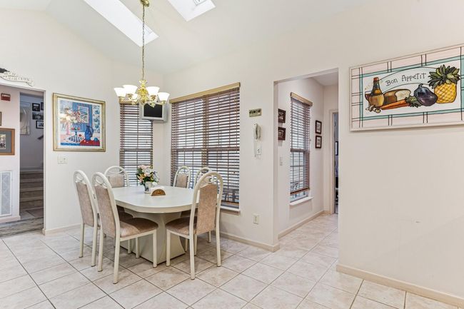 Dining area featuring light tile patterned flooring, baseboards, an inviting chandelier, and lofted ceiling with skylight | Image 32