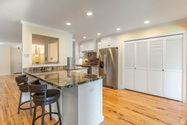 Kitchen featuring a breakfast bar, ornamental molding, light wood-type flooring, a peninsula, and appliances with stainless steel finishes | Image 8