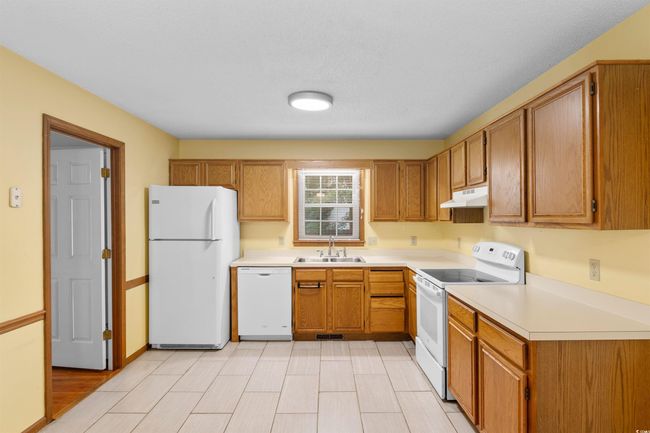 Kitchen featuring white appliances, under cabinet range hood, light countertops, and brown cabinetry | Image 6