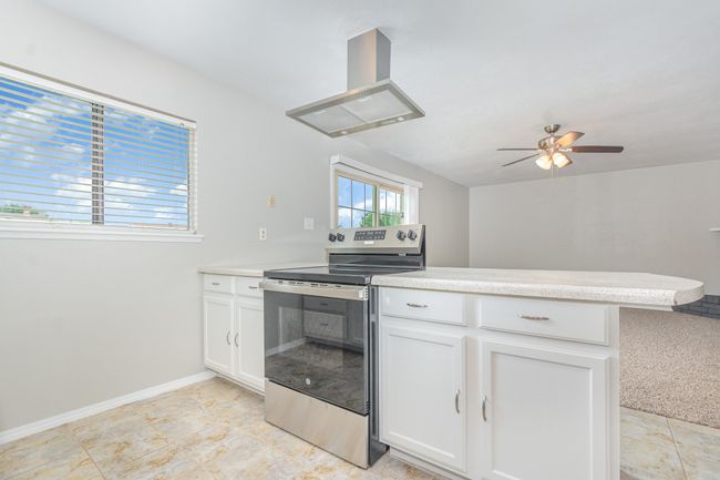 Kitchen featuring stainless steel electric range oven, ceiling fan, light countertops, ventilation hood, and white cabinets | Image 9