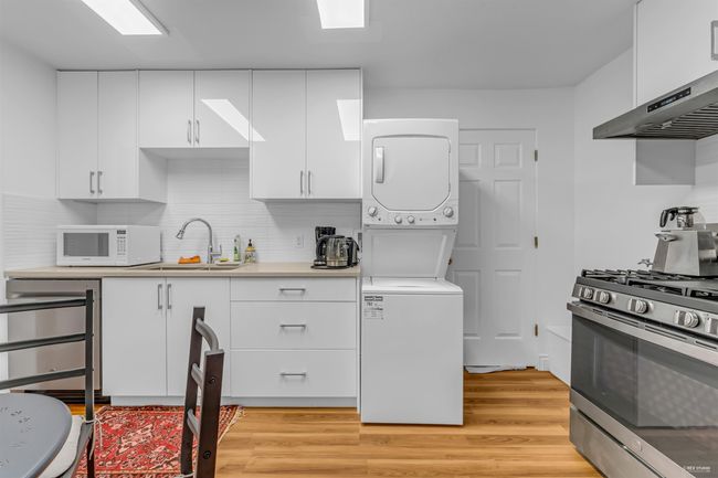 Kitchen featuring stainless steel range with gas stovetop, white microwave, stacked washer and clothes dryer, a sink, and white cabinetry | Image 32