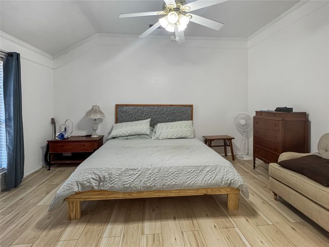 Bedroom with wood finished floors, vaulted ceiling, ornamental molding, and ceiling fan | Image 5
