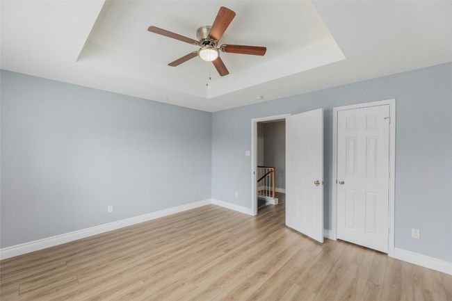 Unfurnished bedroom with a tray ceiling, light wood finished floors, and a ceiling fan | Image 19