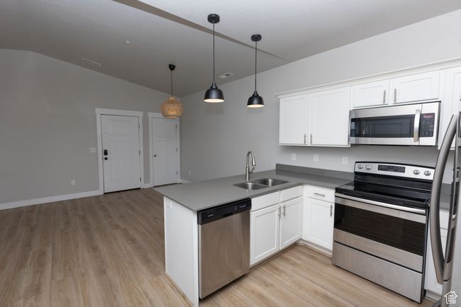 Kitchen featuring stainless steel appliances, a sink, lofted ceiling, light wood-type flooring, and white cabinetry | Image 6