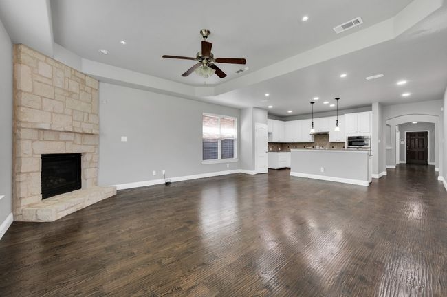 Unfurnished family living area featuring ceiling fan, arched walkways, a fireplace, recessed lighting, and wood floors. | Image 10